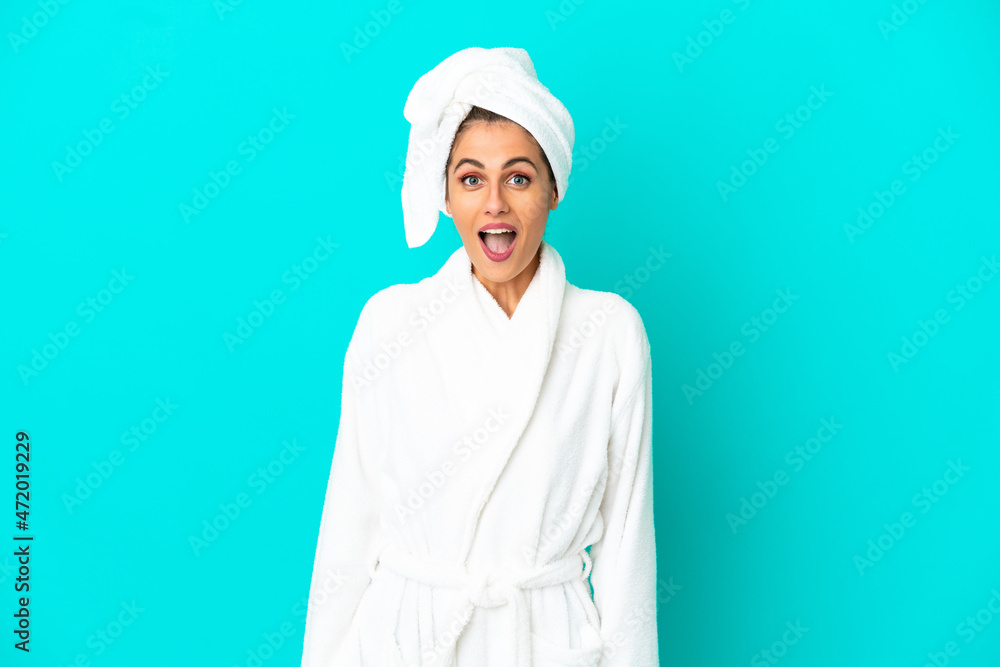 Young woman in a bathrobe over isolated blue background with surprise facial expression Young woman in a bathrobe over isolated blue background with surprise facial expression