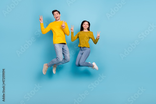 Full size photo of carefree spouses married youth jump make v-sign isolated over blue color background