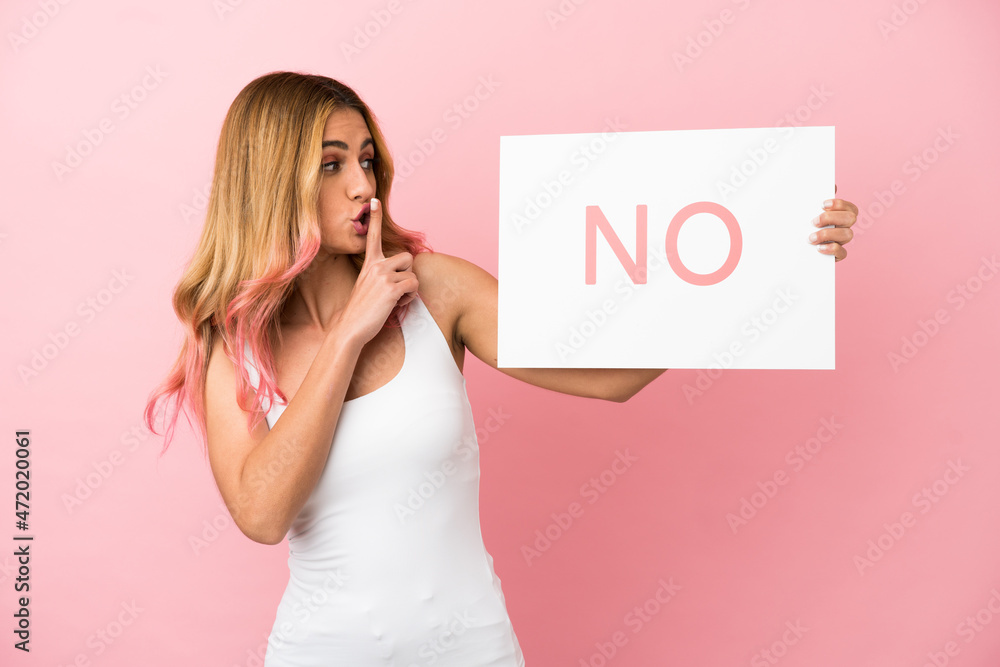 Young woman over isolated pink background holding a placard with text NO doing silence gesture Young woman over isolated pink background holding a placard with text NO doing silence gesture