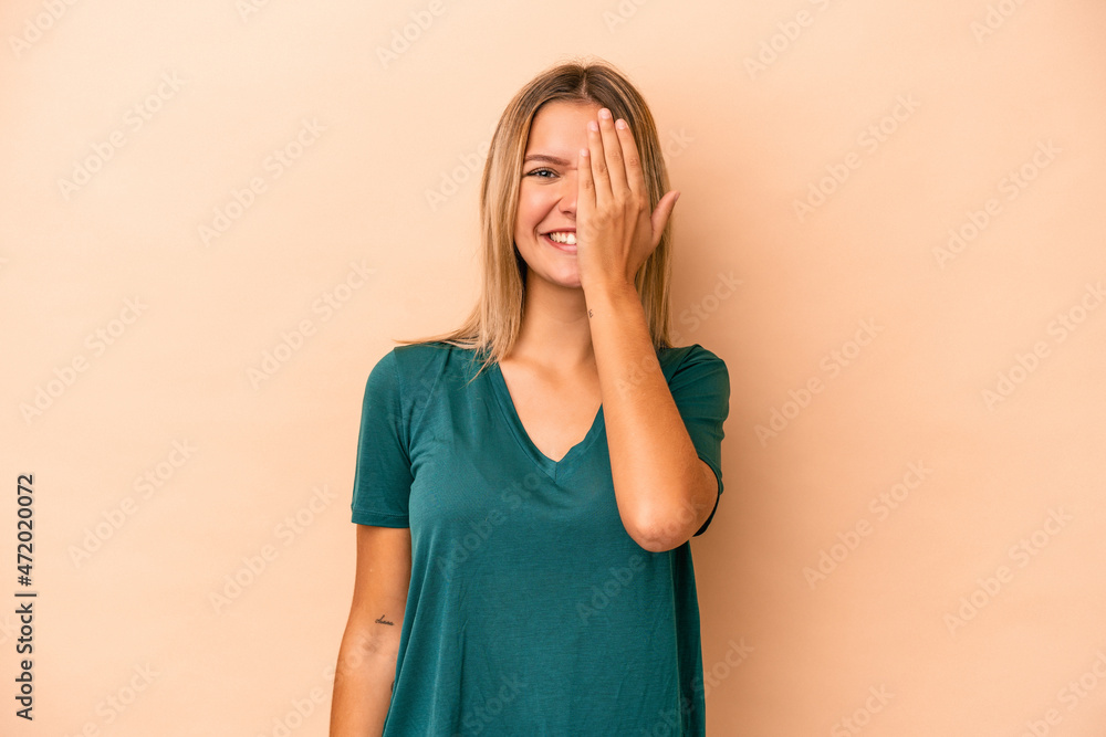 Young caucasian woman isolated on beige background having fun covering half of face with palm. Young caucasian woman isolated on beige background having fun covering half of face with palm.