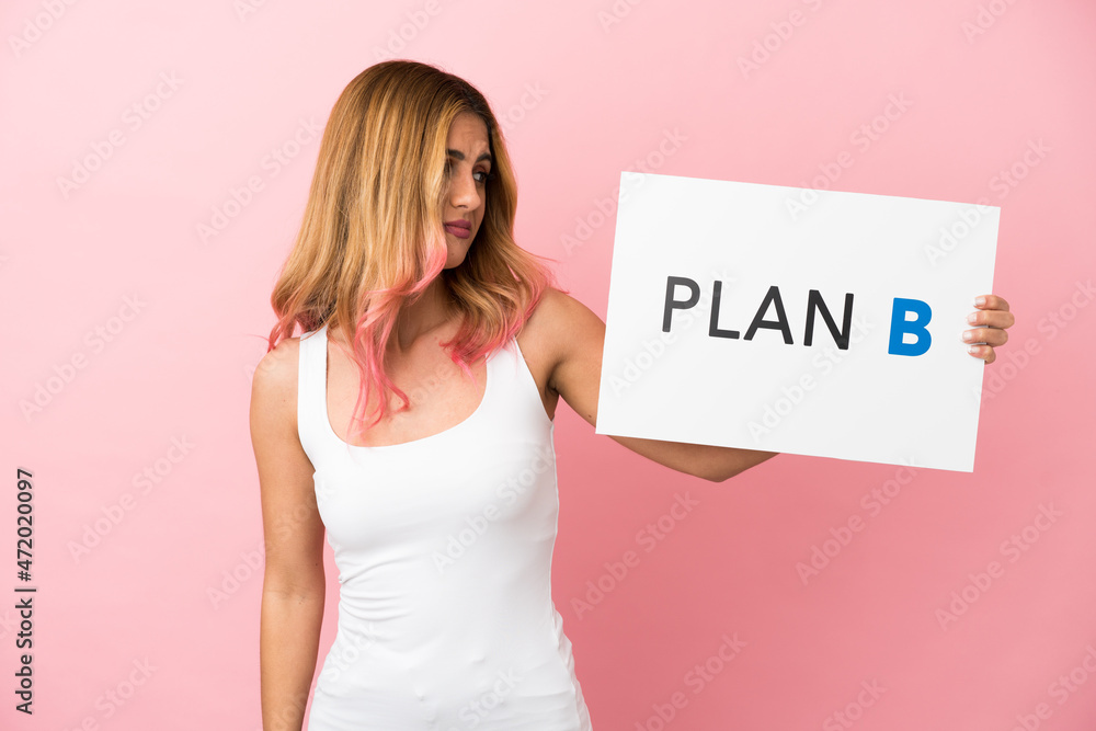 Young woman over isolated pink background holding a placard with the message PLAN B with sad expression Young woman over isolated pink background holding a placard with the message PLAN B with sad expression
