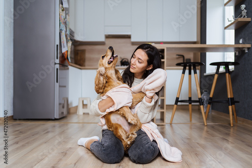 Lovely woman playing with her dog and taking care covering it in a blanket and hugging the pet at home