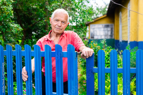 gray haired man in red pollo posing near a blue fence in the village © caftor