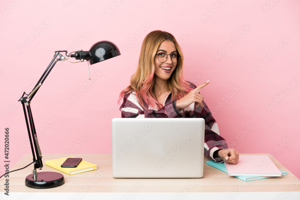 Young student woman in a workplace with a laptop over pink background pointing to the side to present a product Young student woman in a workplace with a laptop over pink background pointing to the side to present a product