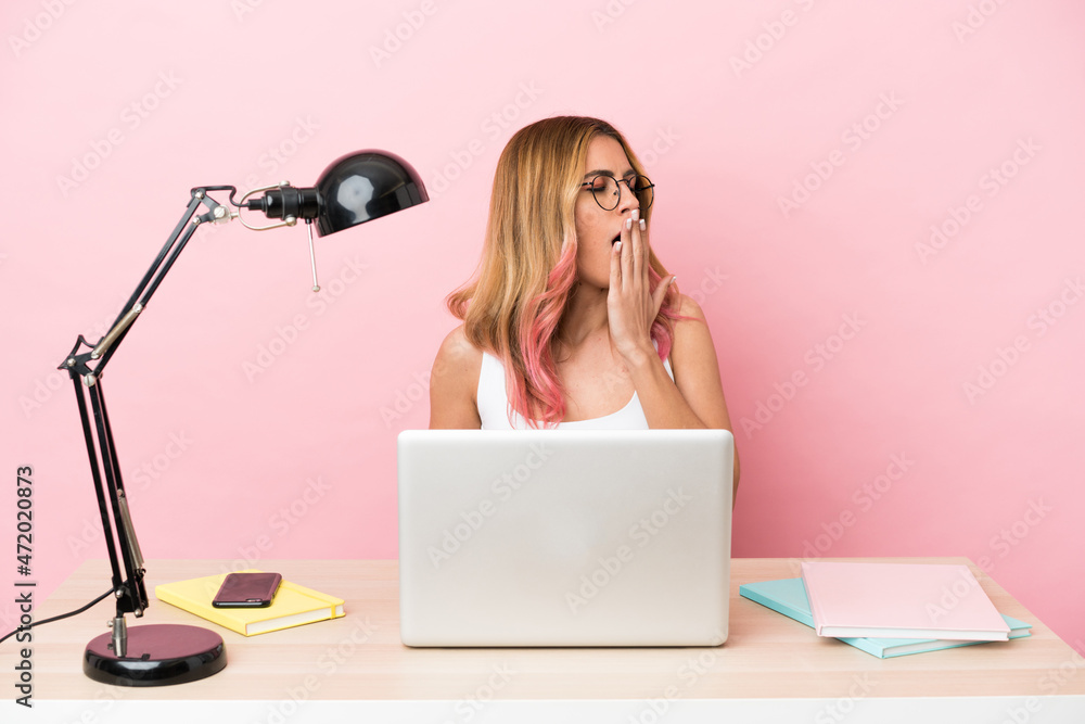 Young student woman in a workplace with a laptop over pink background yawning and covering wide open mouth with hand Young student woman in a workplace with a laptop over pink background yawning and covering wide open mouth with hand