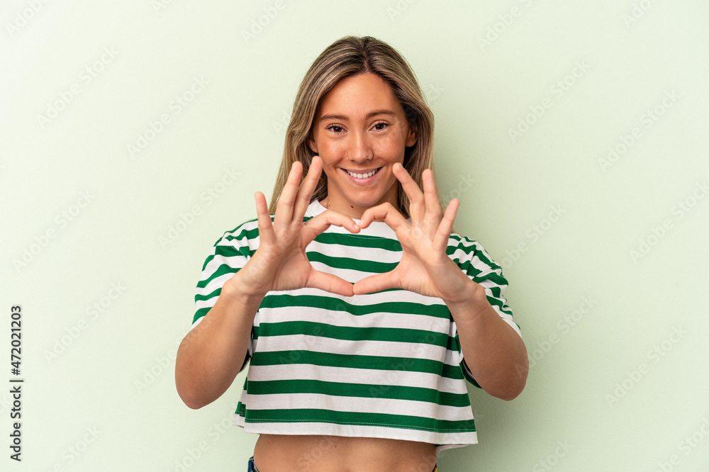 Young caucasian woman isolated on green background smiling and showing a heart shape with hands. Young caucasian woman isolated on green background smiling and showing a heart shape with hands.