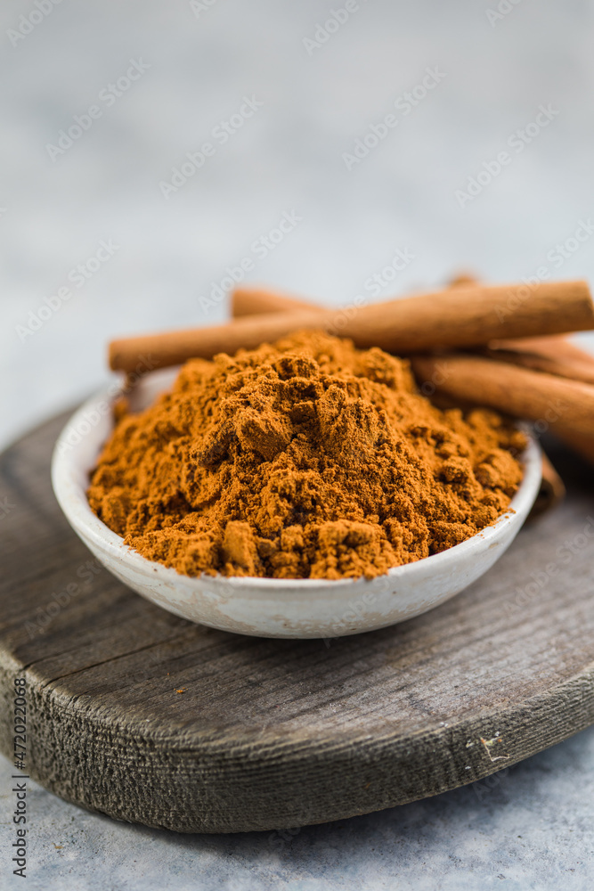 Ceylon cinnamon sticks with cinnamon powder in wooden bowl on concrete background.