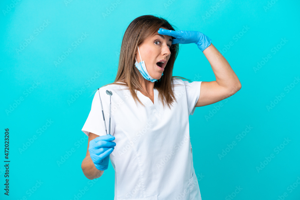 Middle age dentist woman holding tools isolated on blue background Middle age dentist woman holding tools isolated on blue background