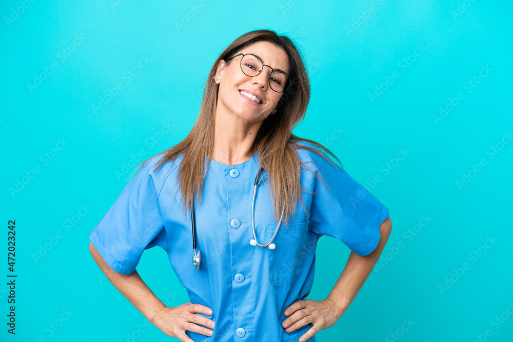 Middle age surgeon woman isolated on blue background posing with arms at hip and smiling Middle age surgeon woman isolated on blue background posing with arms at hip and smiling