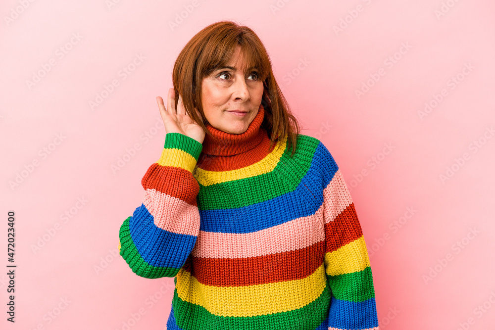 Middle age caucasian woman wearing a multicolor sweater isolated on pink background trying to listening a gossip. Middle age caucasian woman wearing a multicolor sweater isolated on pink background trying to listening a gossip.