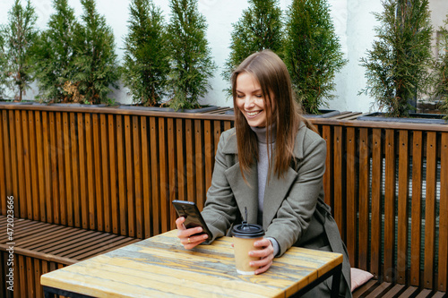 Cuadro en lienzo Beautiful smiling girl with glasses sitting in cafe, holding smartphone in hands