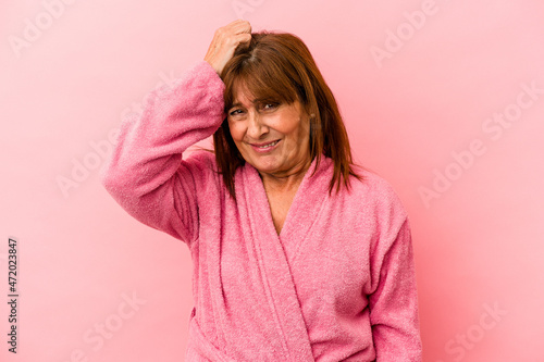 Middle age caucasian woman wearing a bathrobe isolated on pink background being shocked, she has remembered important meeting. © Asier