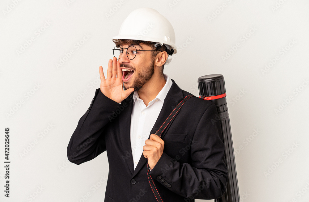 Young mixed race architect man wearing a helmet isolated on grey background shouting and holding palm near opened mouth. Young mixed race architect man wearing a helmet isolated on grey background shouting and holding palm near opened mouth.