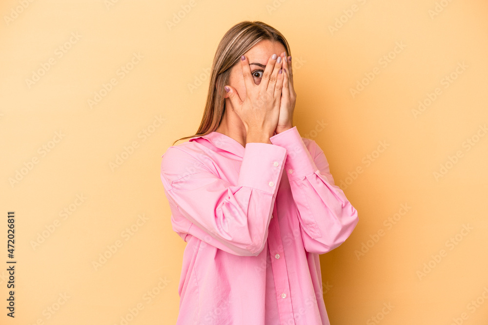 Young caucasian woman isolated on yellow background blink through fingers frightened and nervous. Young caucasian woman isolated on yellow background blink through fingers frightened and nervous.
