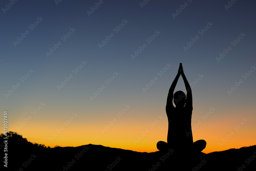 Silhouette of woman doing yoga on mountain sunset sky background.