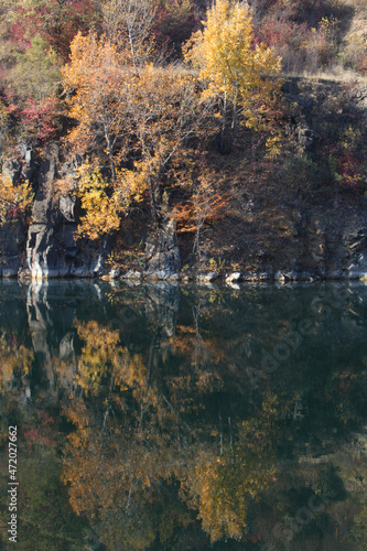 autumn landscape of trees covered with yellow and red leaves on the rocky shore of a mountain lake