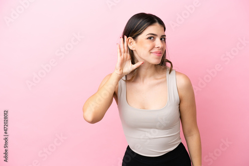 Young Italian woman isolated on pink background listening to something by putting hand on the ear © luismolinero