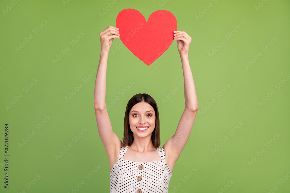 Photo of cool young brunette lady hold heart wear dotted overall isolated on green color background Photo of cool young brunette lady hold heart wear dotted overall isolated on green color background
