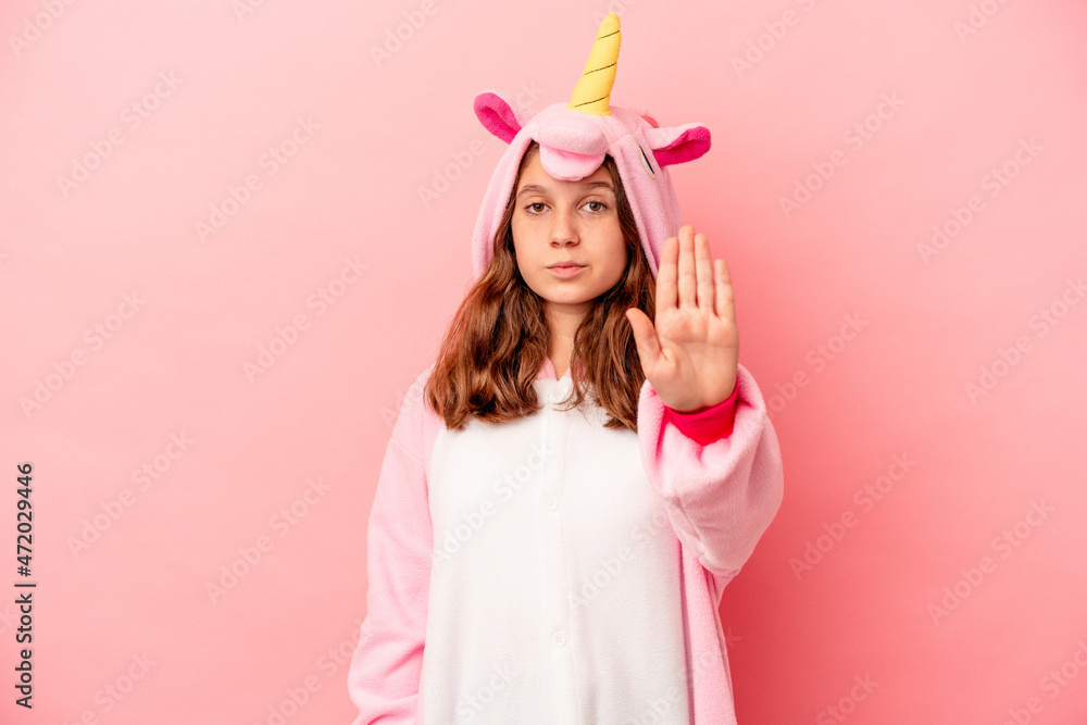 Little caucasian girl wearing a unicorn pajama isolated on pink background standing with outstretched hand showing stop sign, preventing you. Little caucasian girl wearing a unicorn pajama isolated on pink background standing with outstretched hand showing stop sign, preventing you.