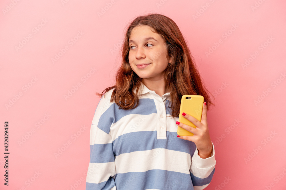 Little caucasian girl holding mobile phone isolated on pink background looks aside smiling, cheerful and pleasant. Little caucasian girl holding mobile phone isolated on pink background looks aside smiling, cheerful and pleasant.