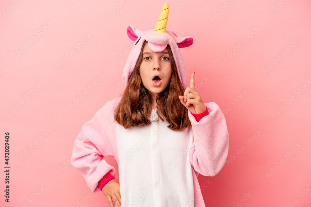 Little caucasian girl wearing a unicorn pajama isolated on pink background having an idea, inspiration concept.