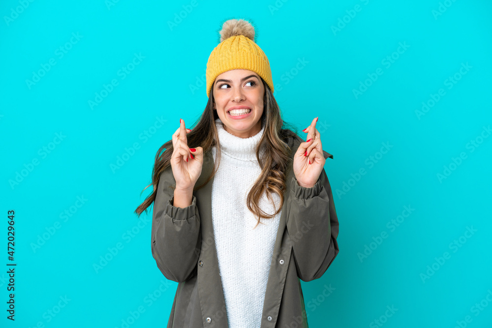 Young Italian woman wearing winter jacket and hat isolated on blue background with fingers crossing Young Italian woman wearing winter jacket and hat isolated on blue background with fingers crossing