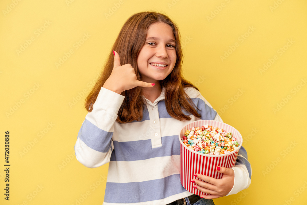 Little caucasian girl holding popcorns isolated on yellow background showing a mobile phone call gesture with fingers.