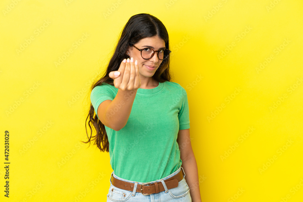Young caucasian woman isolated on yellow background inviting to come with hand. Happy that you came Young caucasian woman isolated on yellow background inviting to come with hand. Happy that you came