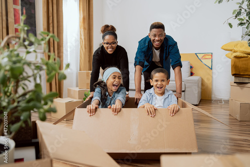 Parents have fun driving cute little son and beautiful daughter in cardboard box play in living room on relocation to new home family feel overjoyed involved in fun activities of moving in together © ABCreative