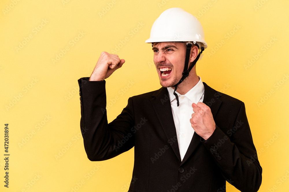 Young architect caucasian man isolated on yellow background raising fist after a victory, winner concept. Young architect caucasian man isolated on yellow background raising fist after a victory, winner concept.