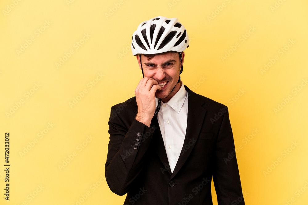 Young caucasian business man wearing a bike helmet isolated on yellow background biting fingernails, nervous and very anxious. Young caucasian business man wearing a bike helmet isolated on yellow background biting fingernails, nervous and very anxious.