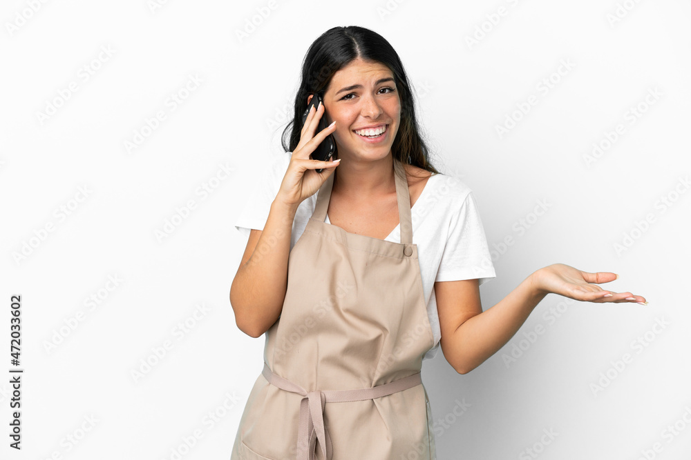Restaurant waiter over isolated white background keeping a conversation with the mobile phone with someone Restaurant waiter over isolated white background keeping a conversation with the mobile phone with someone
