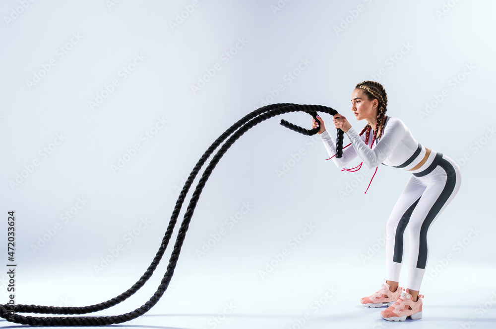 Athletic young woman with battle rope doing exercise in functional training fitness gym. Girl working out arms and cardio using battle rope for fit exercises.