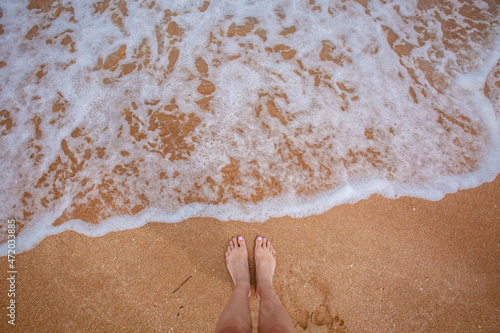Photography Woman's legs stand by the sea waves on a golden beach