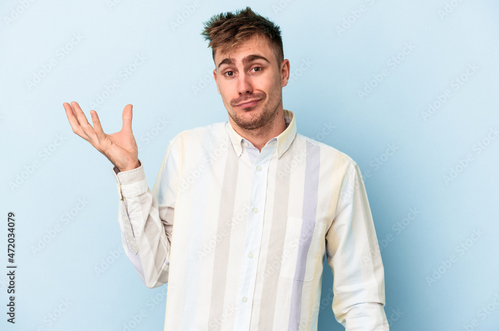 Young caucasian man isolated on blue background doubting and shrugging shoulders in questioning gesture. Young caucasian man isolated on blue background doubting and shrugging shoulders in questioning gesture.