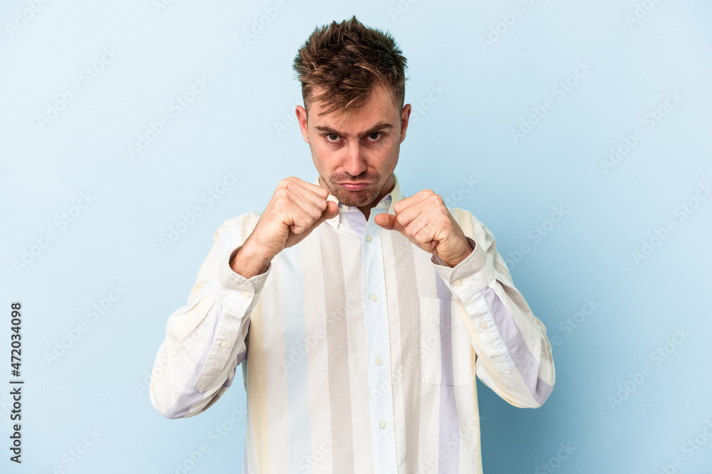 Young caucasian man isolated on blue background showing fist to camera, aggressive facial expression. Young caucasian man isolated on blue background showing fist to camera, aggressive facial expression.