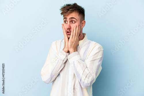 Young caucasian man isolated on blue background scared and afraid.