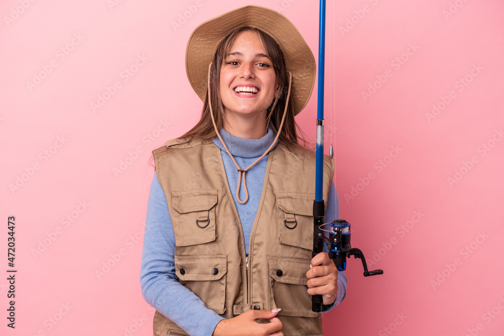 Young caucasian fisherwoman holding a rod isolated on pink background laughing and having fun. Young caucasian fisherwoman holding a rod isolated on pink background laughing and having fun.