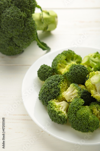 Bunch of fresh green broccoli on white bowl on white wooden background.