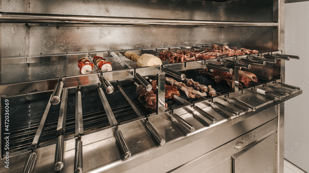 Different meats are cooked on skewers on electric grill in restaurant.