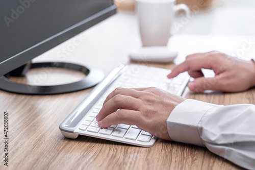 A man typing on white desktop keyboard on wood table business work concept in office