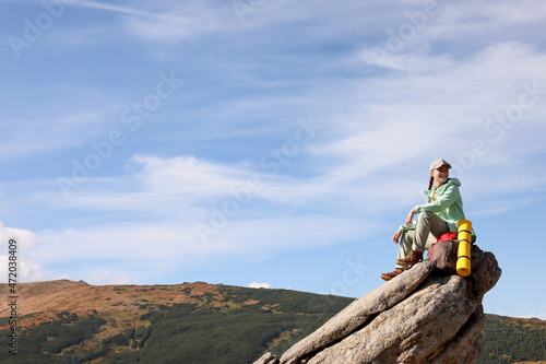 Young woman with backpack and sleeping mat on cliff in mountains. Space for text