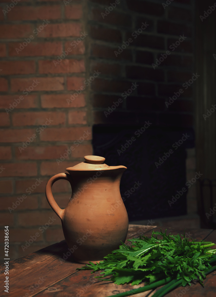 Old rustic wine jug on a wooden table.Ceramic clay terracotta jug.the composition is filled with greenery. conceptual photo with reflection of national color.dark background,lots of advertising space Old rustic wine jug on a wooden table.Ceramic clay terracotta jug.the composition is filled with greenery. conceptual photo with reflection of national color.dark background,lots of advertising space