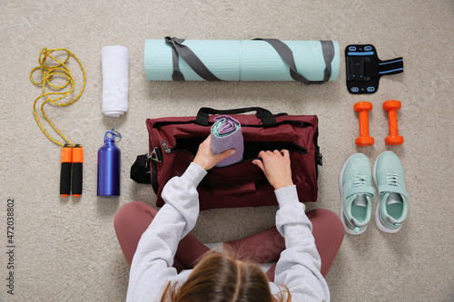 Fototapeta Naklejka Na Ścianę i Meble -  Woman packing sports stuff for training into bag on floor, top view