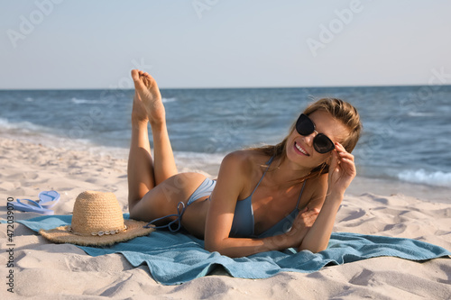 Attractive woman with sunglasses sunbathing on beach towel near sea