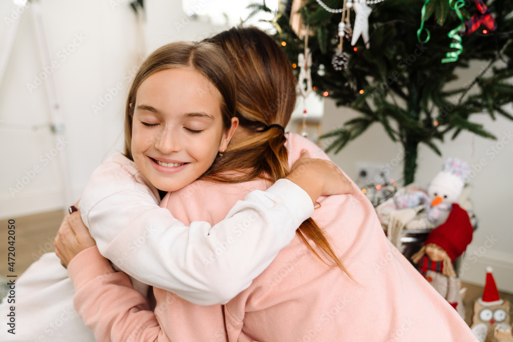 Naklejka premium White mother and daughter hugging while decorating christmas tree