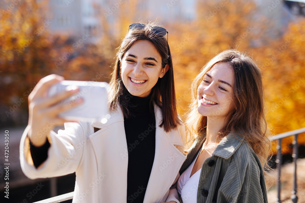 Teenage girl taking selfie with friend through smart phone in autumn park Teenage girl taking selfie with friend through smart phone in autumn park