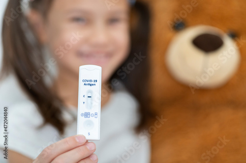Smiling girl with teddy bear showing rapid diagnostic test result photo