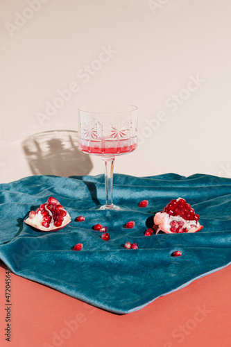 Creative arrangement  of pomegranate on a blue plush fabric. Minimal vintage concepet of a wine crystal glass on a pastel background.