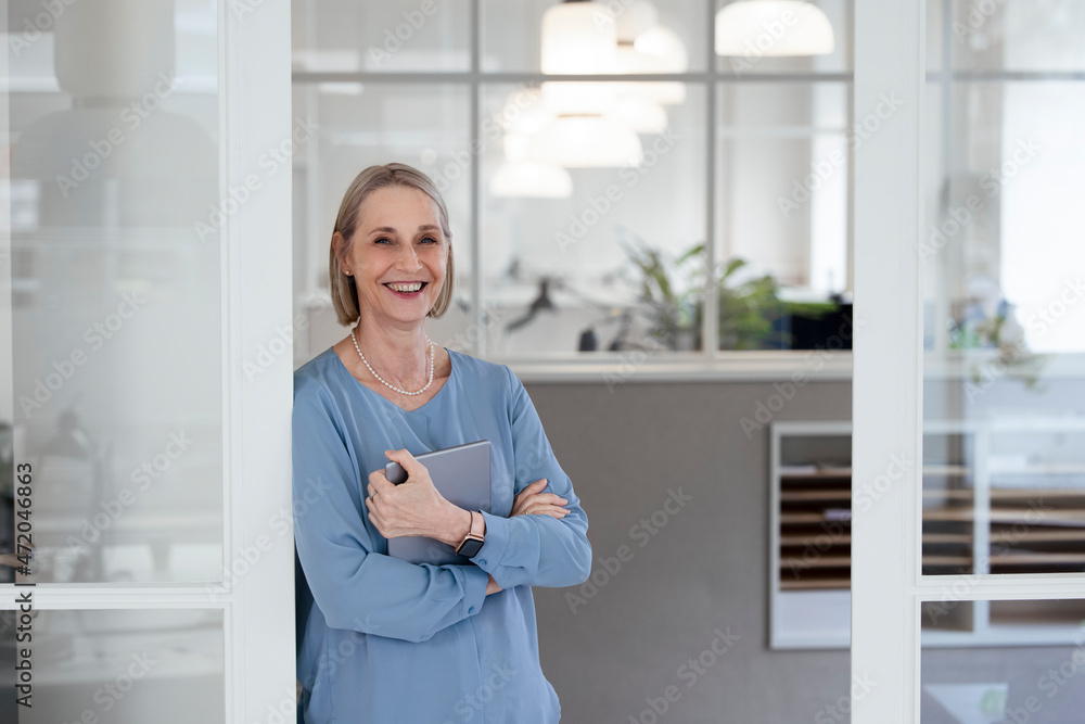 Smiling businesswoman with tablet PC leaning on office door Smiling businesswoman with tablet PC leaning on office door